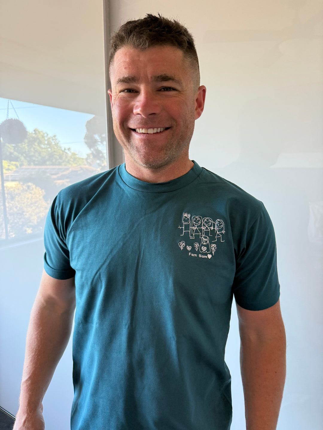Dad wearing his daughter's family drawing embroidered on a teal RK Threads tee